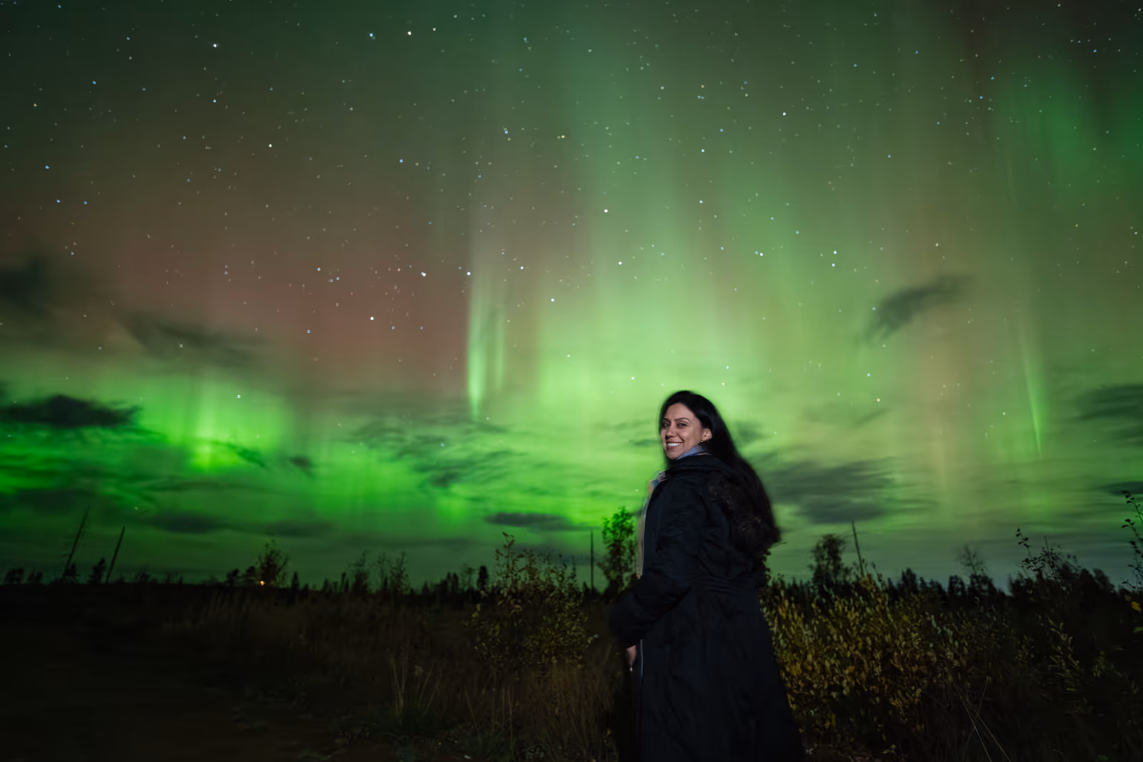 Woman looking back at towering green aurora pillars over the autumn Lapland landscape